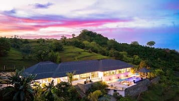 A modern house with a swimming pool, surrounded by lush greenery and hills.