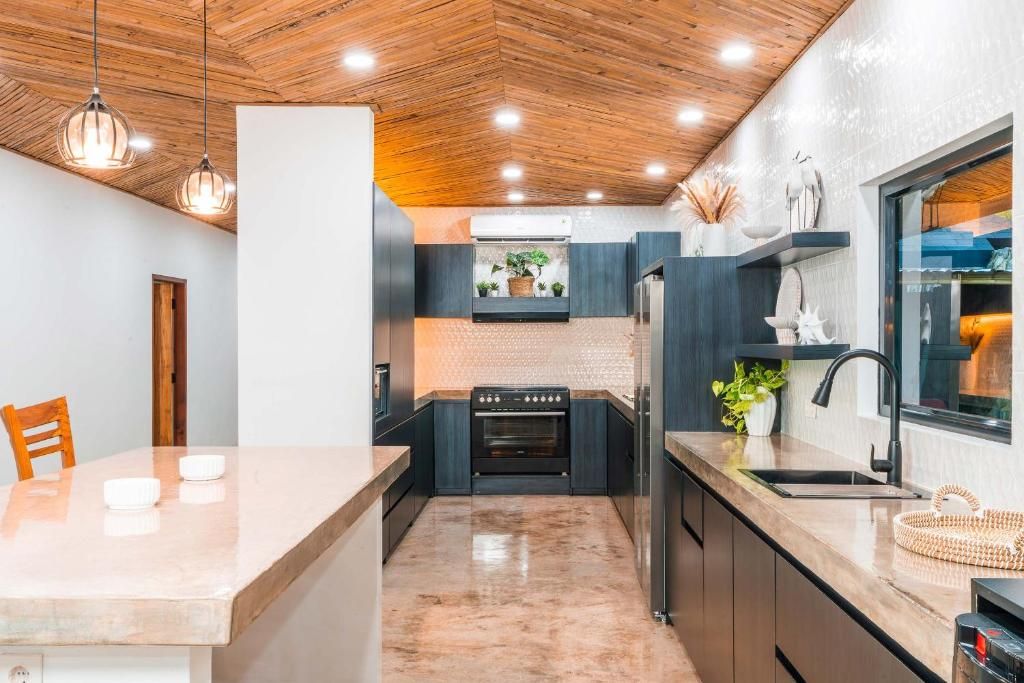 A modern kitchen with a central island, dark cabinetry, and a wooden ceiling.