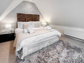 A bedroom with a bed, two bedside tables, a radiator, and a textured wall. - The Genoa Suite at Whitehall (Whitby)