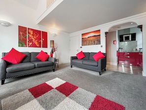 A living room with two grey sofas, red cushions, a red and white rug, and artwork on the walls. - The Genoa Suite at Whitehall (Whitby)