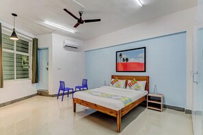 Un dormitorio con una cama, dos sillas azules, un ventilador de techo y un equipo de aire acondicionado.