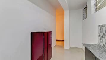 Un pasillo estrecho con un refrigerador rojo, una pared blanca con un diseño decorativo de azulejos y una puerta que da a otra habitación.