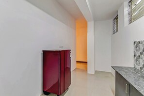 A narrow hallway with a red refrigerator, a white wall with a decorative tile pattern, and a door leading to another room. - Capital O Elite Stay Jp Nagar  (Bangalore)