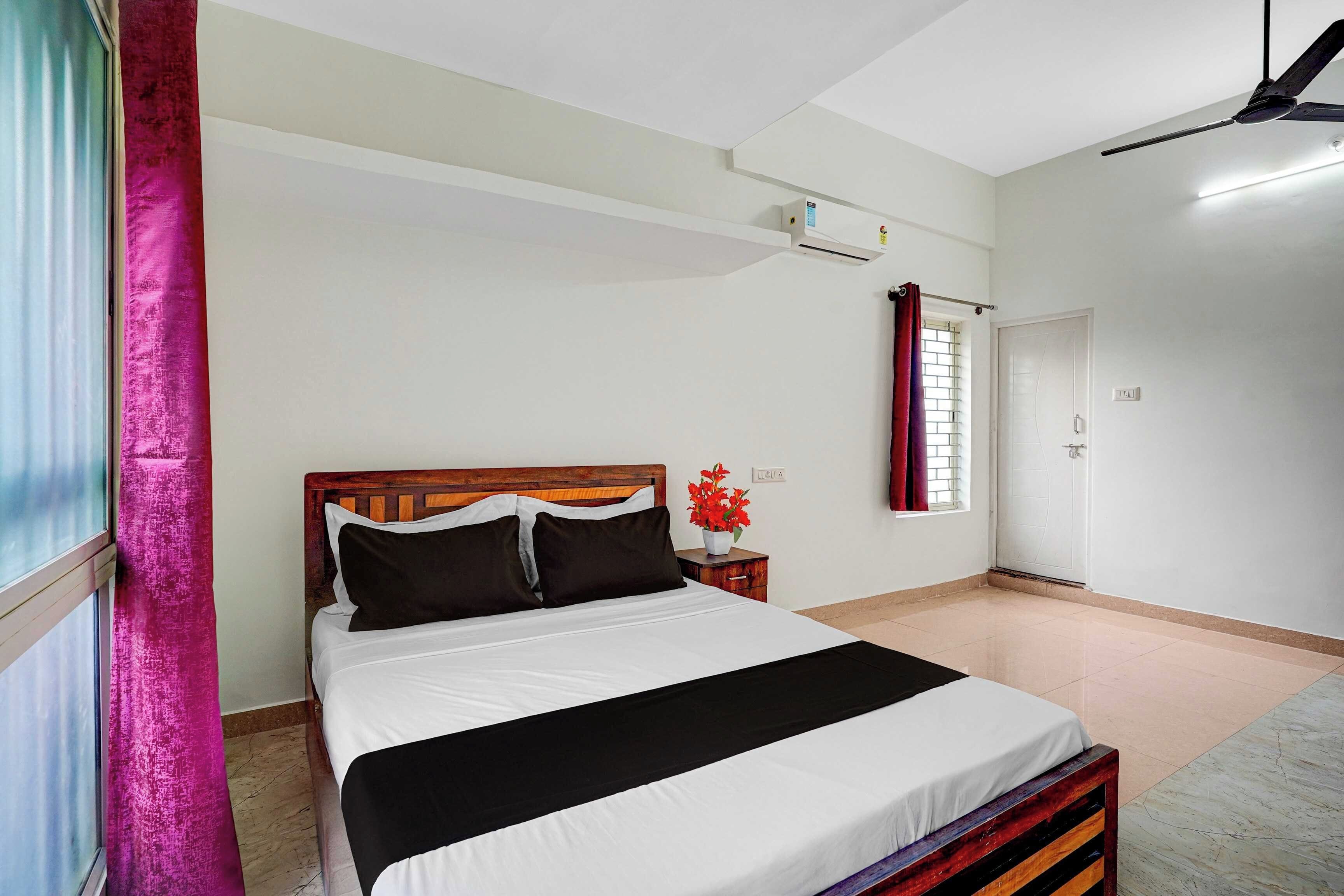 Un dormitorio con cama, mesita de noche, ventana con cortinas y una puerta.