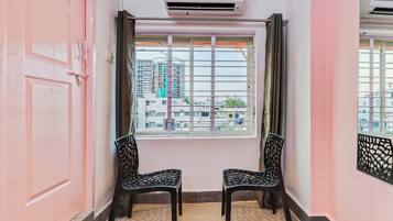 Una habitación con una pared rosa, un ventanal con vistas a edificios, dos sillas y un equipo de aire acondicionado.