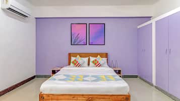 Un dormitorio con cama, dos mesitas de noche, cabecera de madera, pared morada, dos cuadros enmarcados y un armario.
