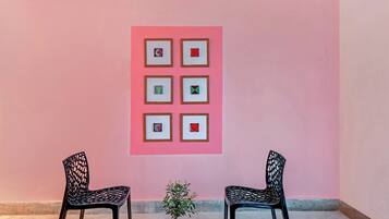 Una habitación con una pared rosa, dos sillas negras y una pequeña planta en maceta.