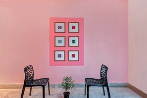 Una habitación con una pared rosa, dos sillas negras y una pequeña planta en maceta.