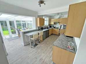 A modern kitchen with a central island, wooden cabinets, and a large window overlooking a garden. - 2 bedroom accommodation in Bodham, near Sheringham (Bodham, near Sheringham)