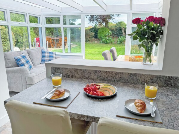 Un plateau de petit-déjeuner avec des croissants, des fruits et du jus d’orange, disposé sur un comptoir de cuisine, avec vue sur un jardin.