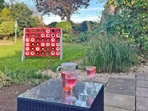 A garden setting with a table featuring a pitcher and two glasses, surrounded by greenery and a decorative board. - 2 bedroom accommodation in Bodham, near Sheringham (Bodham, near Sheringham)