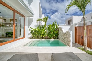 A modern outdoor pool area with a stone wall, tropical plants, and a wooden gate. - Kembali 2BR Private Pool Villa Balangan (Badung)