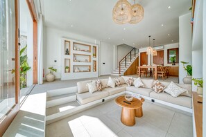 A modern living room with a sectional sofa, a coffee table, and a staircase leading to a dining area. - Kembali 2BR Private Pool Villa Balangan (Badung)