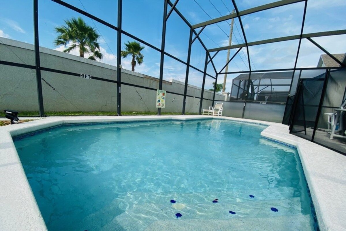 Ein rechteckiger Swimmingpool mit klarem, blauem Wasser, umgeben von einer weißen Poolterrasse und einer Glaseinfriedung.