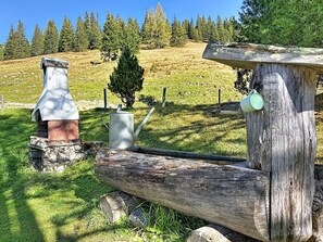 A rustic outdoor setting with a wooden structure, a metal container, and a small tree. - Schneehitzalmhütte by Interhome (Wörschach)
