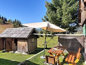 Eine rustikale Holzhütte mit geneigtem Dach, einem Picknicktisch und einem großen Sonnenschirm, der Schatten spendet.