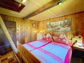 Ein Zimmer aus Holz mit einem Bett, einem Gemälde, einer Uhr und einer Lampe.