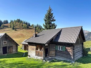 Eine rustikale Holzhütte mit geneigtem Dach, einem Schornstein und einer kleinen Veranda mit Geländer.