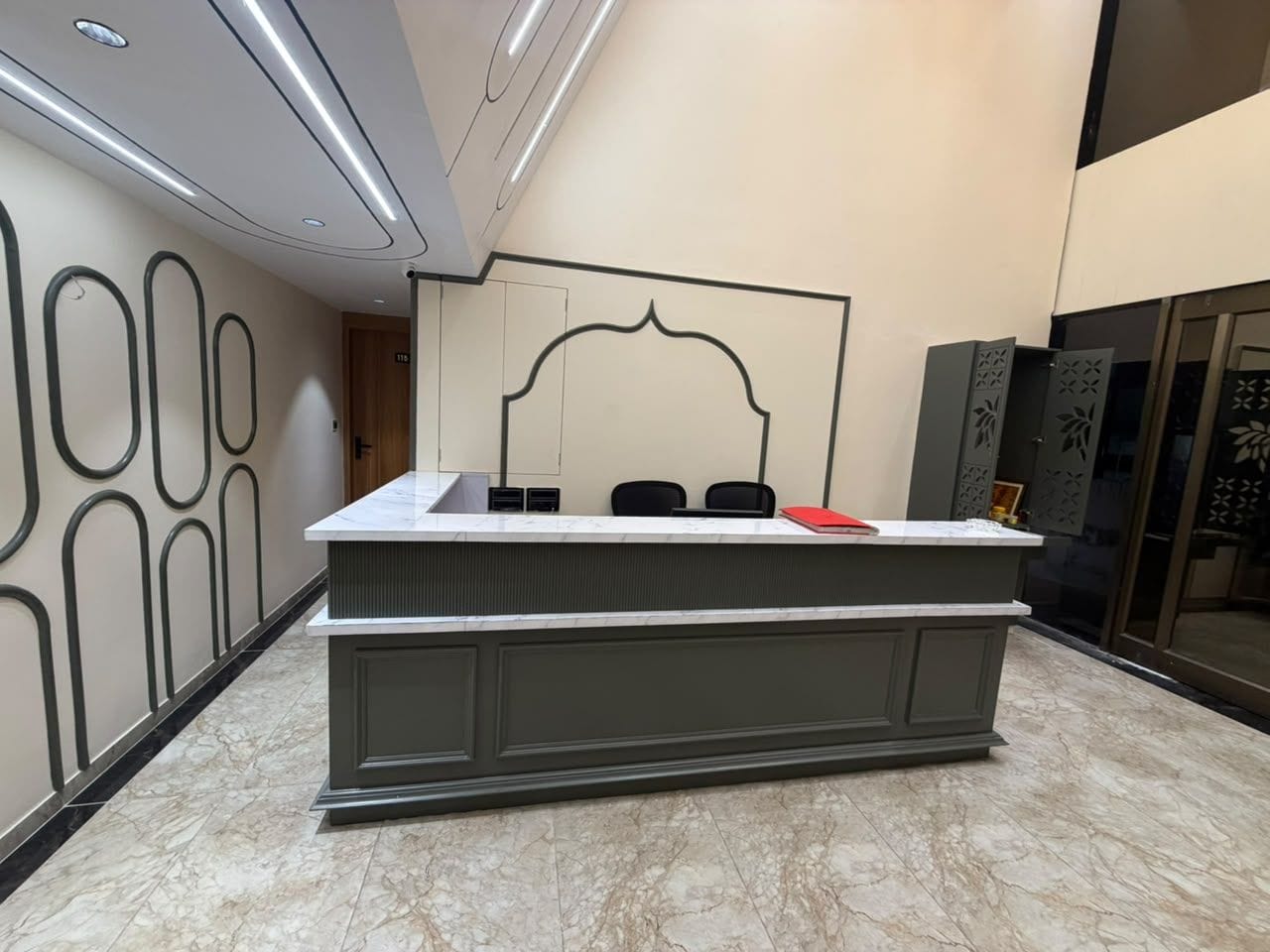 Un mostrador de recepción con piso de mármol, una pared con diseños geométricos y una puerta al fondo.