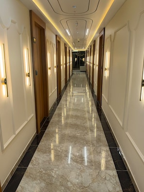 Un pasillo de hotel con puertas a ambos lados, suelo de mármol y apliques de pared que proporcionan luz.