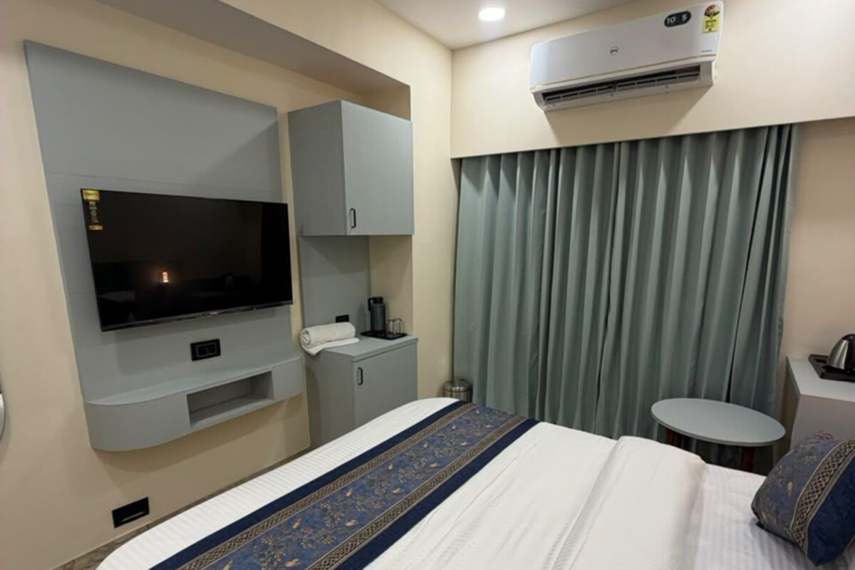 Habitación de hotel con cama, televisor, escritorio, silla, aire acondicionado y ventana con cortinas.