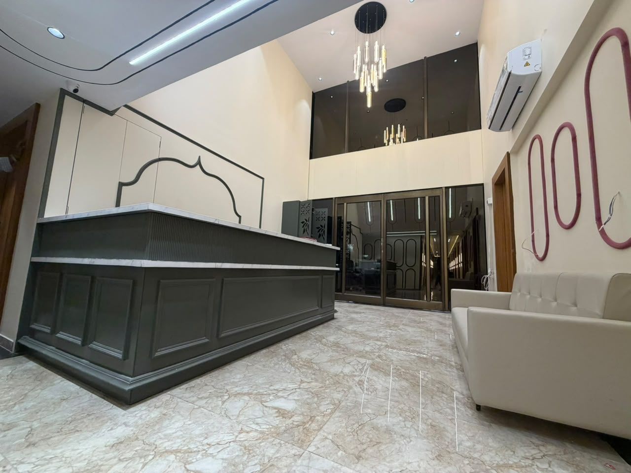 A modern lobby with a reception desk, a white sofa, and a chandelier.