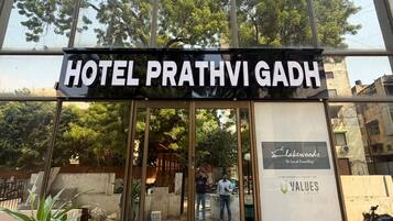 De ingang van Hotel Prathvi Gadh, met een helder zicht op het interieur door de glazen deuren.
