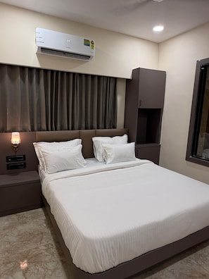 Habitación de hotel con cama, aire acondicionado, mesita de noche con lámpara, armario y ventana.