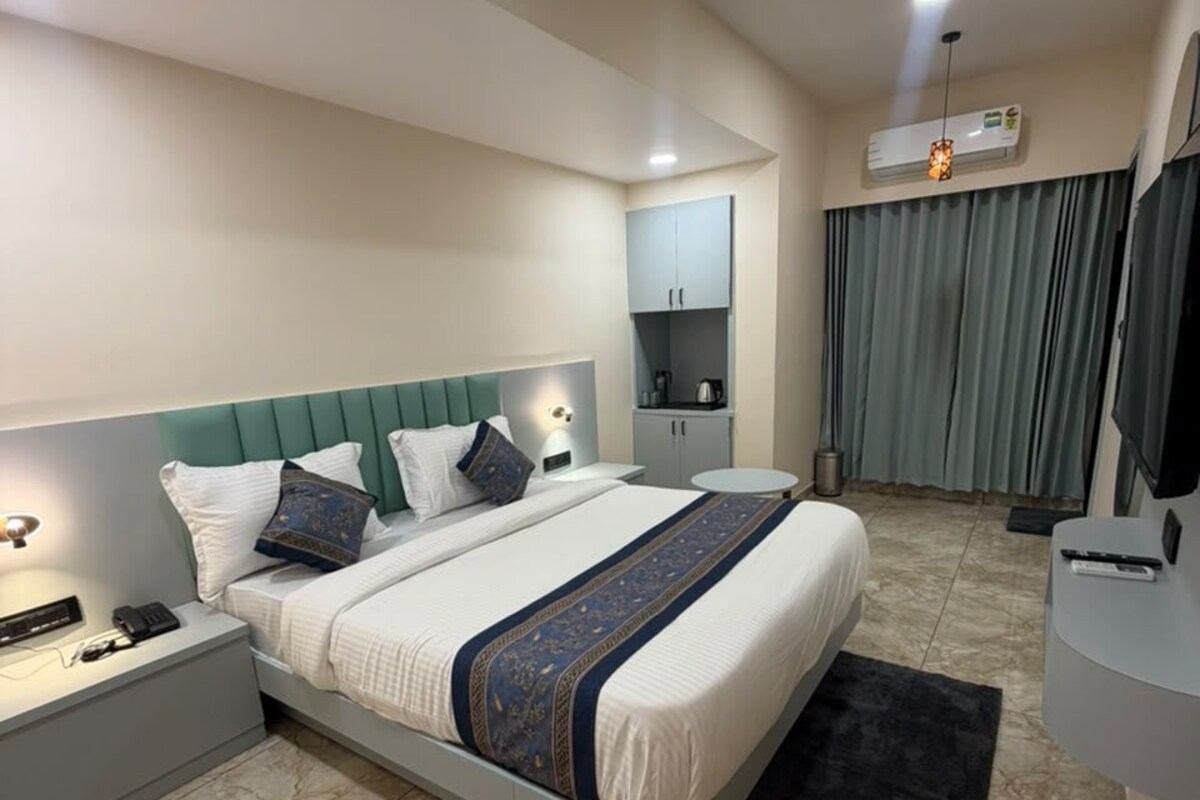 Una habitación de hotel moderna con cama, mesitas de noche, escritorio, silla, televisor y aire acondicionado.