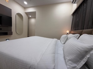 Una habitación de hotel con una cama grande, un televisor de pantalla plana montado en la pared y una mesita de noche.