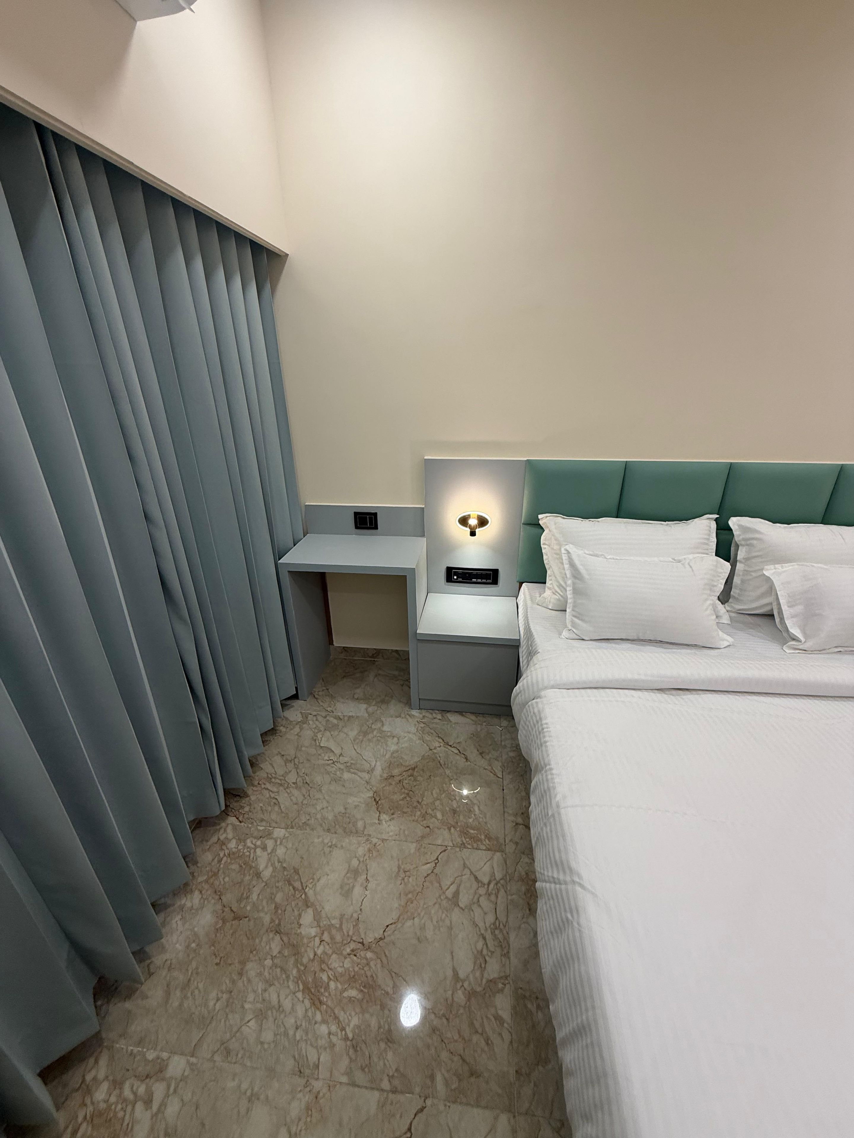 Een hotelkamer met een bed, nachtkastje, bureau en gordijn.