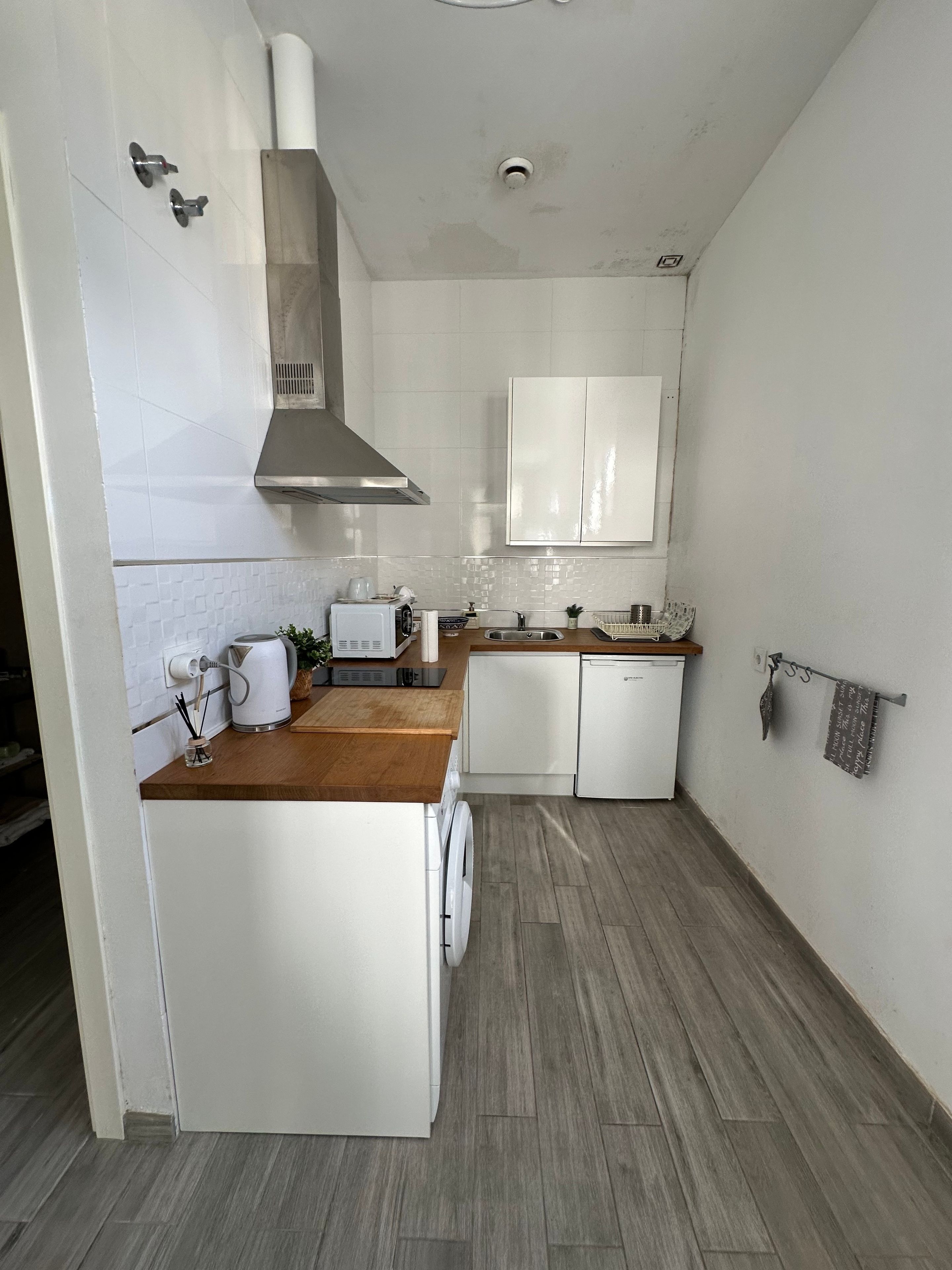 Een moderne keuken met witte kasten, een houten aanrecht, een ingebouwde oven en een roestvrijstalen afzuigkap.