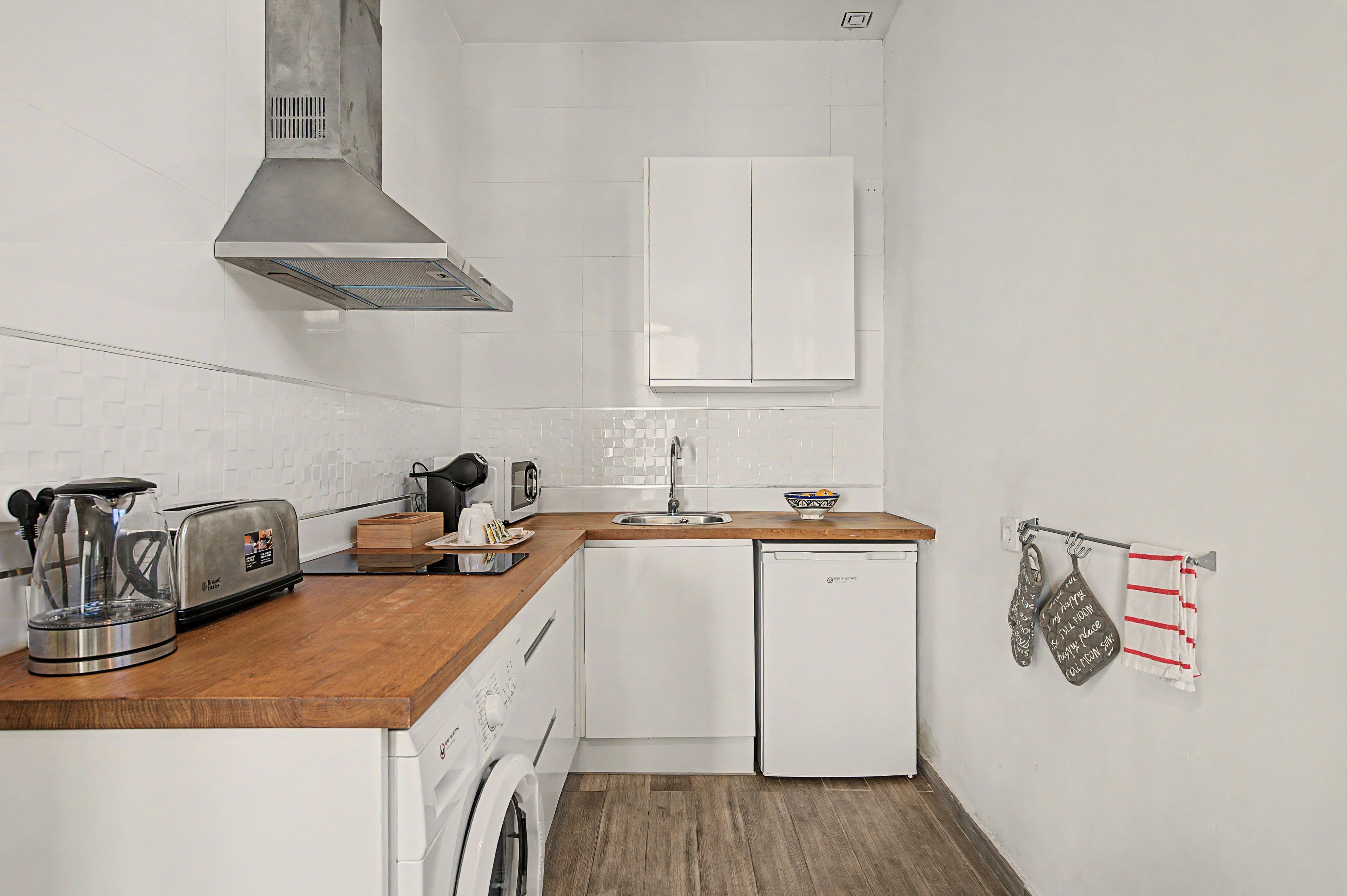 Una cocina compacta con tostadora, hervidor, microondas, lavaplatos y lavamanos.