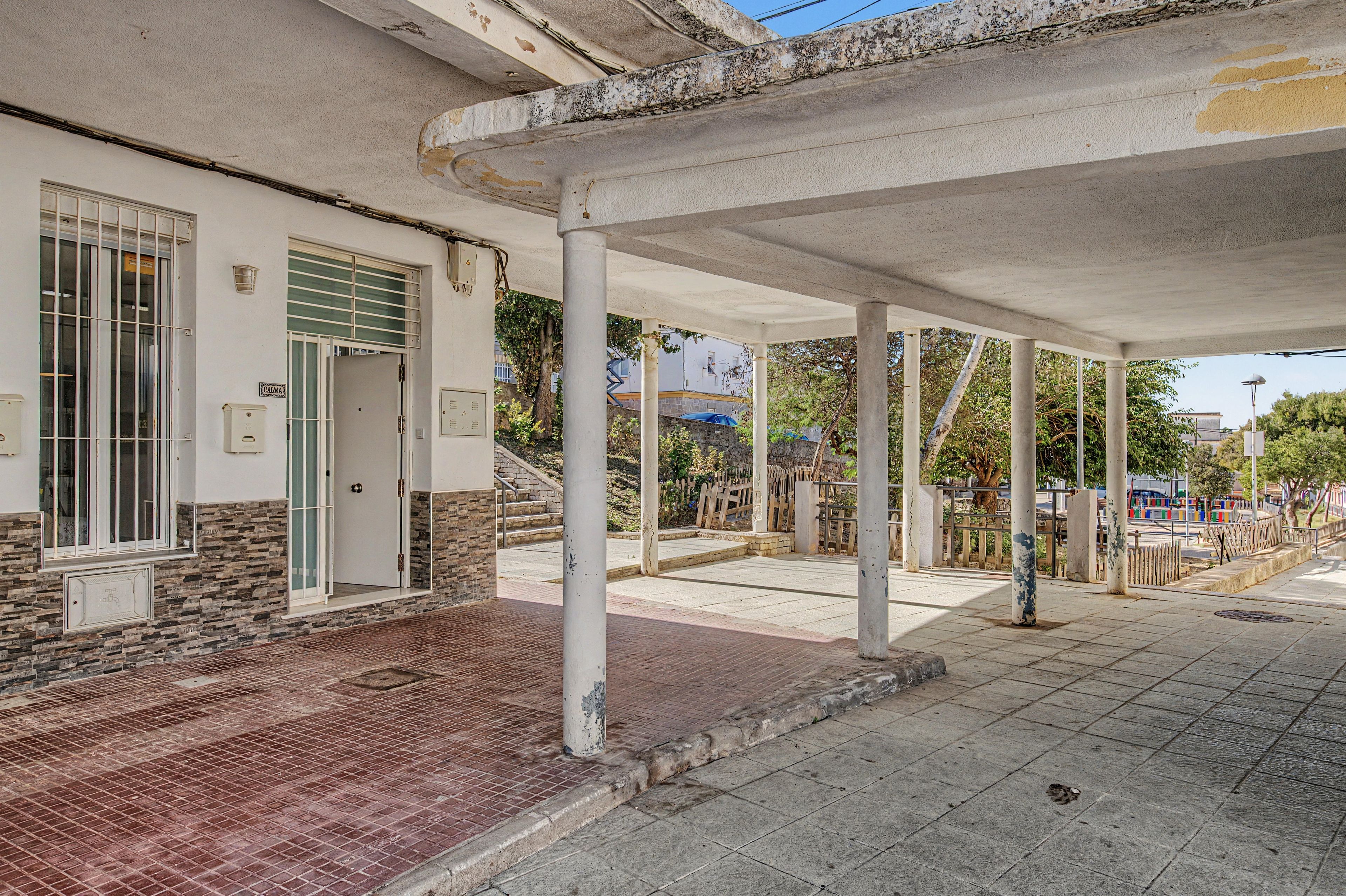 A covered outdoor area with a building entrance, a stone wall, and a metal gate.