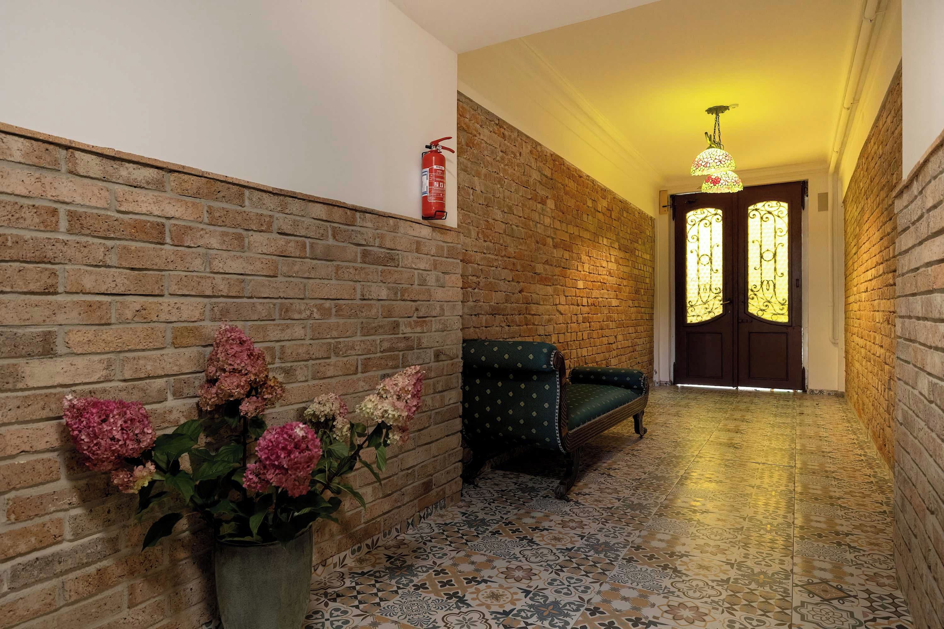 A hallway with a brick wall, a fire extinguisher mounted on it, a bench, and a door with decorative glass panels.