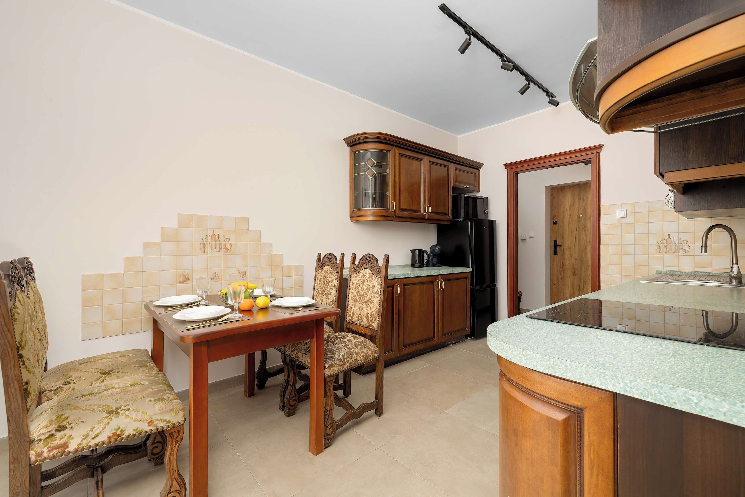 A compact kitchen with wooden cabinets, a dining table set for four, and a modern induction cooktop.