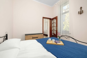 Un dormitorio con una cama, un aparador, una ventana con cortinas y una bandeja con tazas y un libro.