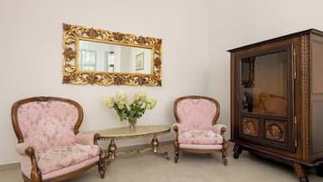 Una stanza con due poltrone decorate, un tavolino, uno specchio con una cornice elaborata e un mobile con anta in vetro.