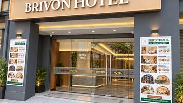L’extérieur de l’hôtel Brivon, avec sa façade moderne, son entrée en verre et ses affiches promotionnelles.