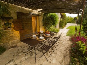 An outdoor dining area with stone walls, a wooden door, and a table set for four with chairs. - Charming Holiday Home With Pool - 904 ANS (Ansouis)