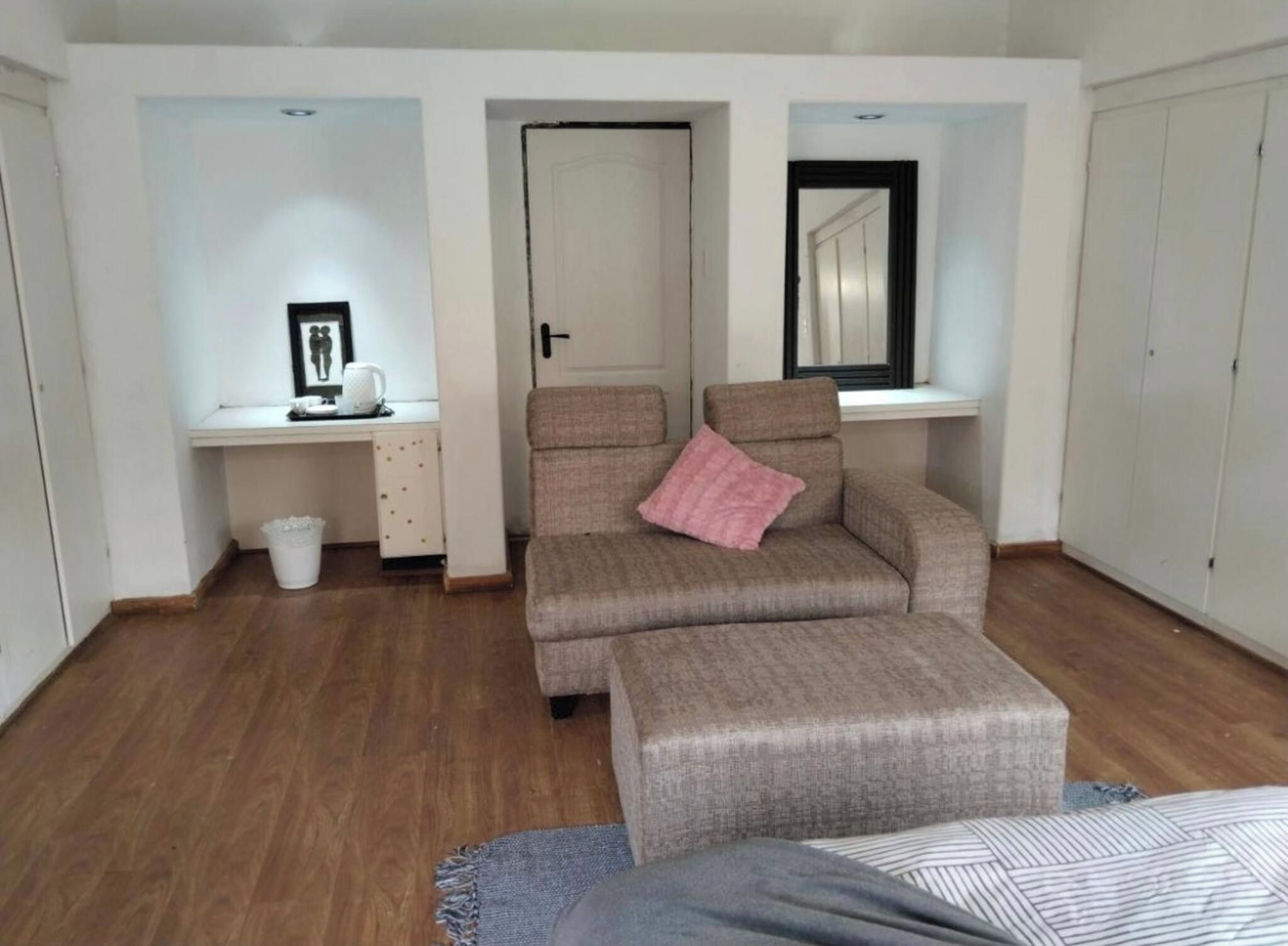 Een knus ingerichte kamer met een bank, een tafeltje, een spiegel en een kledingkast.