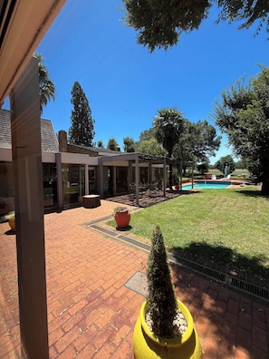 Un patio con piscina, un patio de ladrillo y un edificio con ventanas grandes.