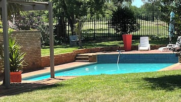 A swimming pool surrounded by a brick wall, a pergola, and a grassy lawn.