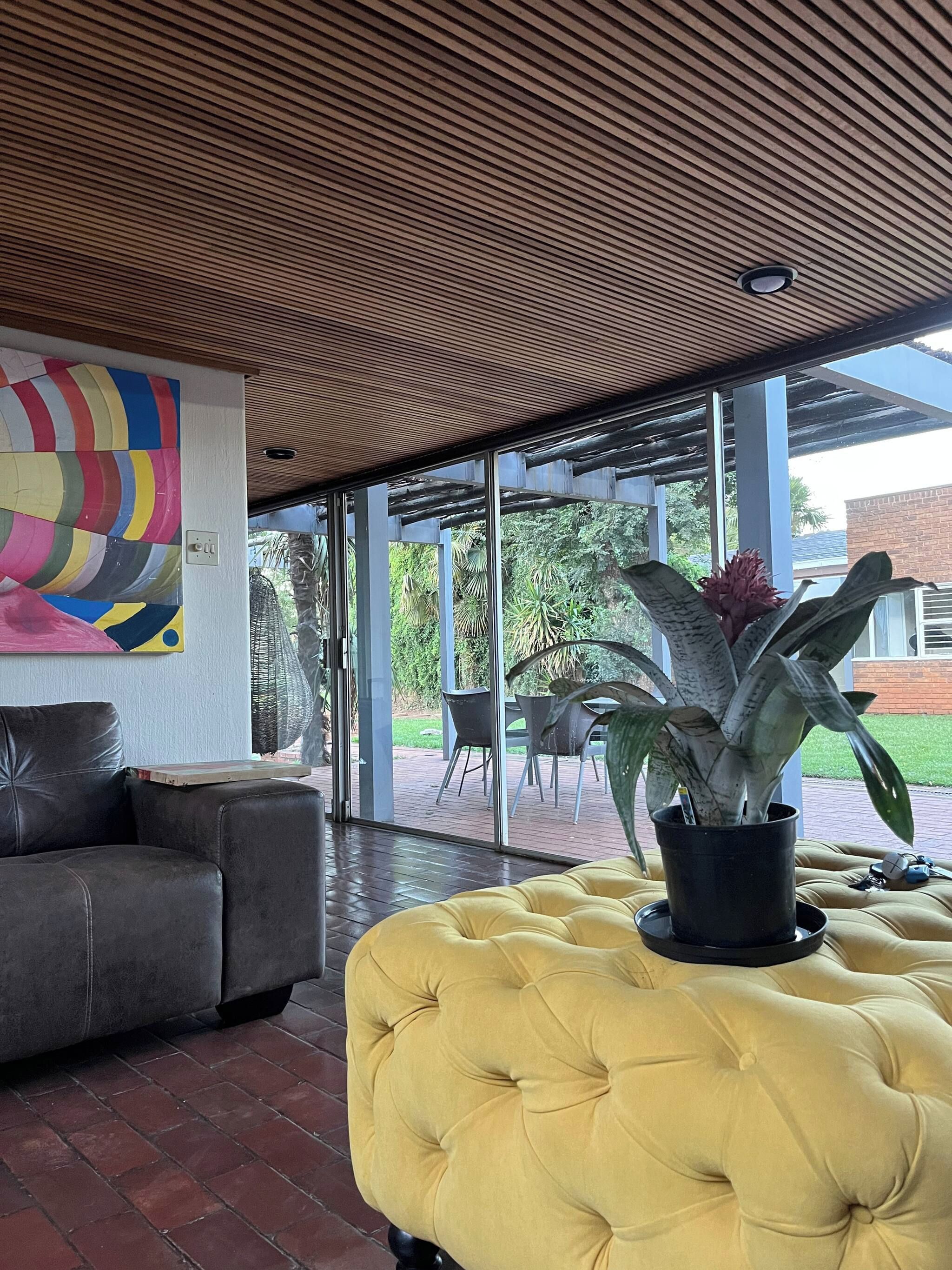 A modern interior with a yellow tufted sofa, a black leather couch, and a colorful abstract mural.
