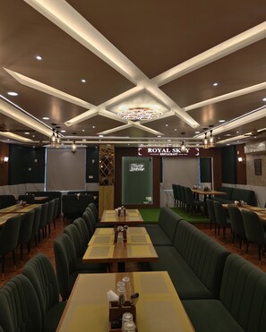 Un interior de restaurante con una zona de comedor central, mesas tipo cabina y un letrero que dice 'Royal Sky Restaurant'.