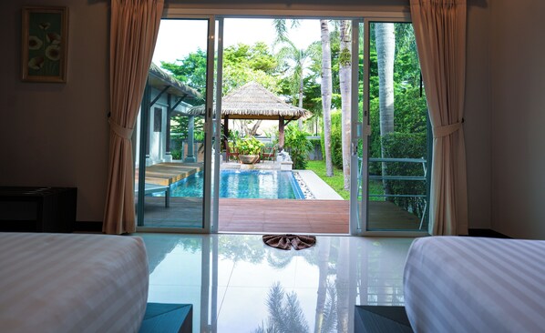 Une chambre d’hôtel avec une porte vitrée donnant sur un espace piscine, une structure à toit de chaume et une vue sur une végétation luxuriante.