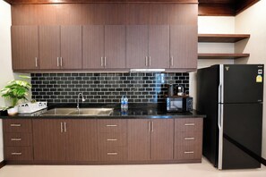 A modern kitchen with dark wooden cabinets, a black tiled backsplash, stainless steel appliances, and a black refrigerator.