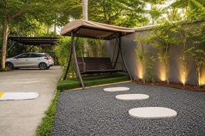 A garden with a swing set, a car, and a paved path with stepping stones.