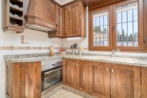 A kitchen with wooden cabinets, a built-in oven, a granite countertop, and a window with a view. - Villa Alejandro in Sayalonga. Located on a quiet, sunny private estate (Sayalonga)