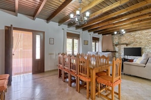 A dining area with a wooden table and chairs, a chandelier, and a stone wall. - Villa Alejandro in Sayalonga. Located on a quiet, sunny private estate (Sayalonga)